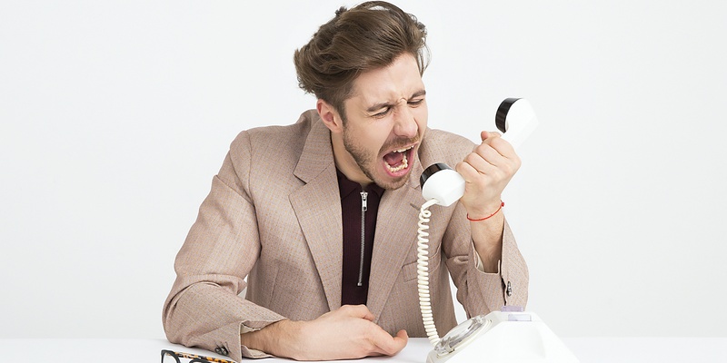 Workplace bullying: a man shouting into a desk telephone