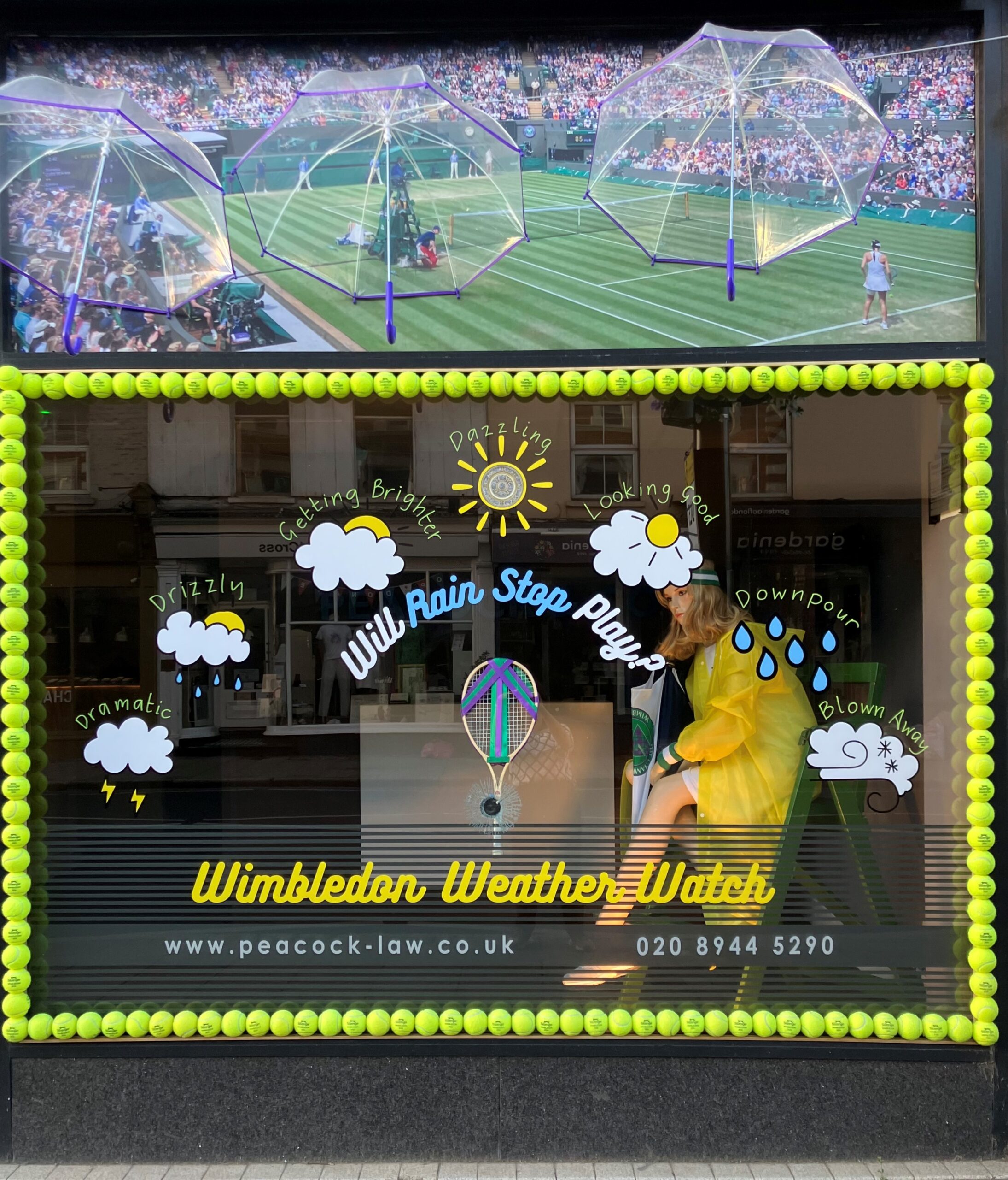 Wimbledon Tennis window for 2024 Wimbledon weather watch barometer with model in an umpire's chair wearing poncho.